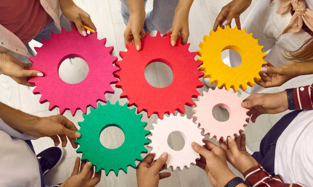 Team or group of men and women standing in circle joining gears holding colorful cogs. Cropped shot. Teamwork, integration, business, education, success concept background