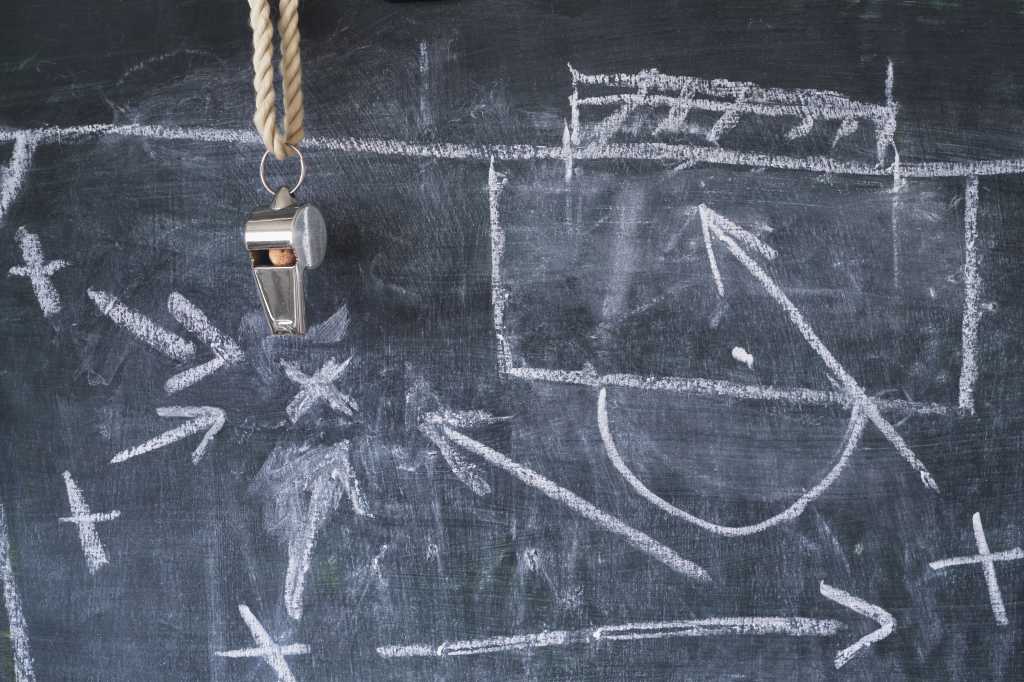 Tactical diagram of soccer plays in white chalk on a blackboard.