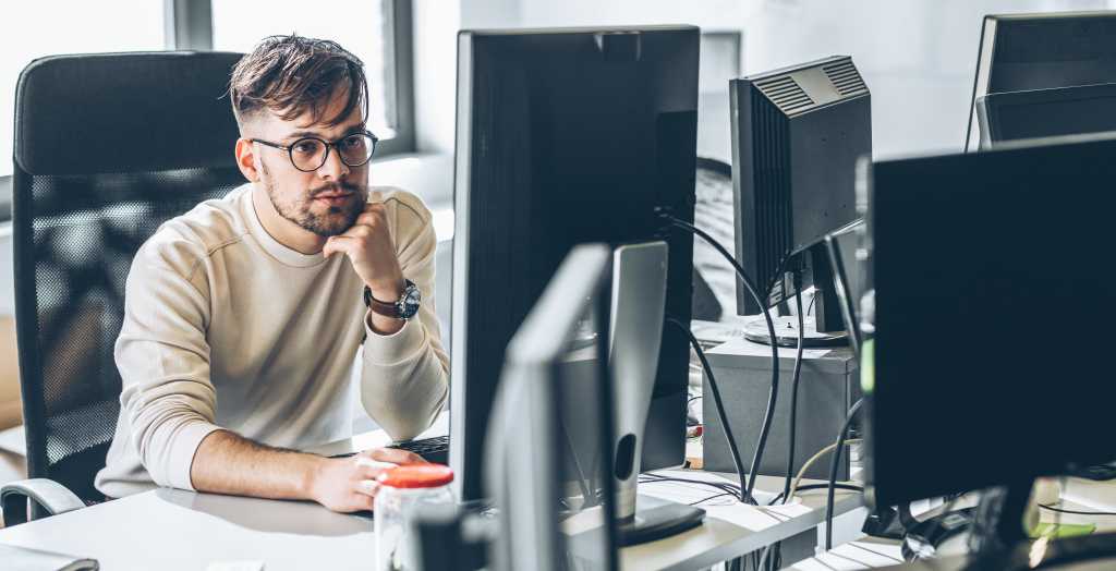 Programmer sitting at the desk in his office and trying to solve problem of new code.