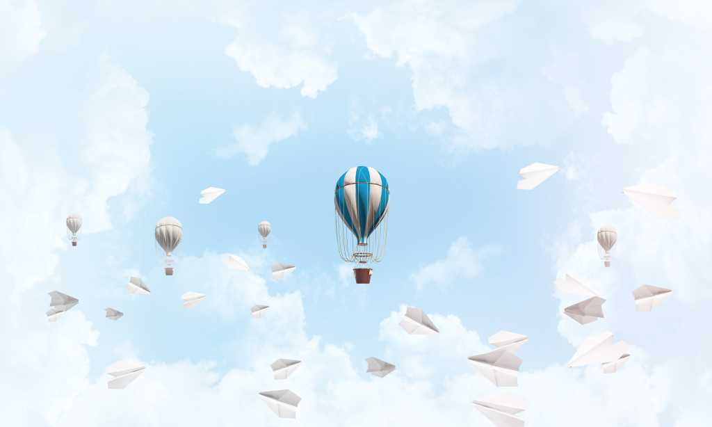 shutterstock 1117048970 colorful balloons flying among paper planes and against a cloudy blue sky