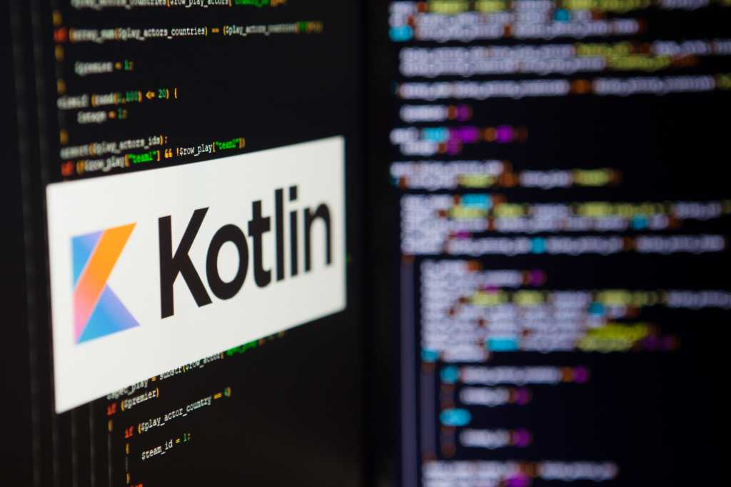 A computer screen shows the Kotlin logo against a backdrop of code.