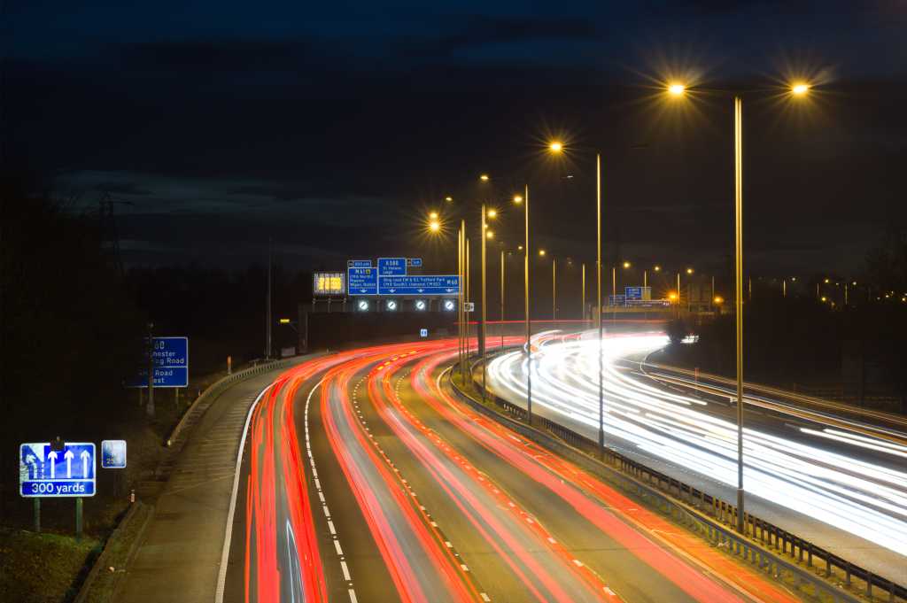 Smart motorway in England, UK with light trails signifying busy traffic at rush hour. The NSL symbols under the gantry sign signify an end to speed restrictions.